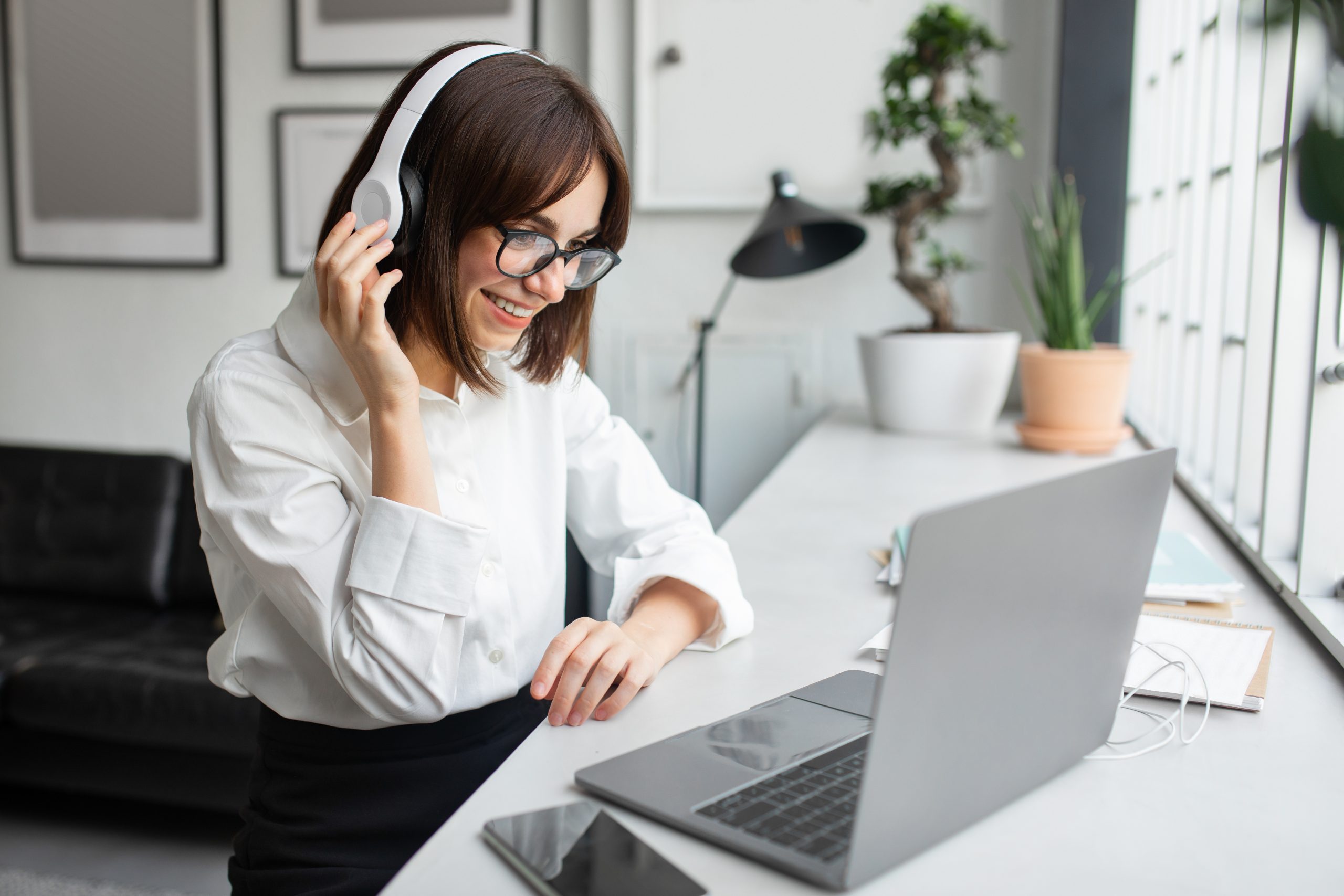 Positive european businesswoman in headphones communication with client working on computer in modern office